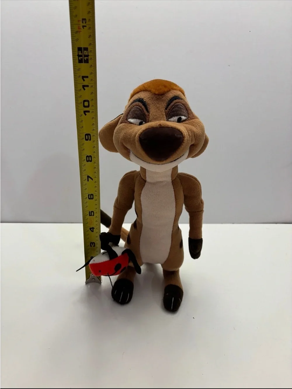 Disney The Lion King Timon plush toy holding a small red ladybug